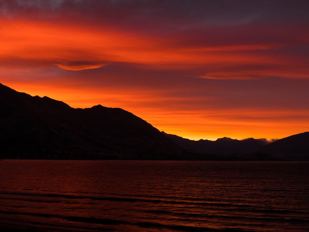 Une voiture de sport rouge roulant sur une route sinueuse au bord du lac Léman, avec les Alpes en arrière-plan au coucher du soleil.