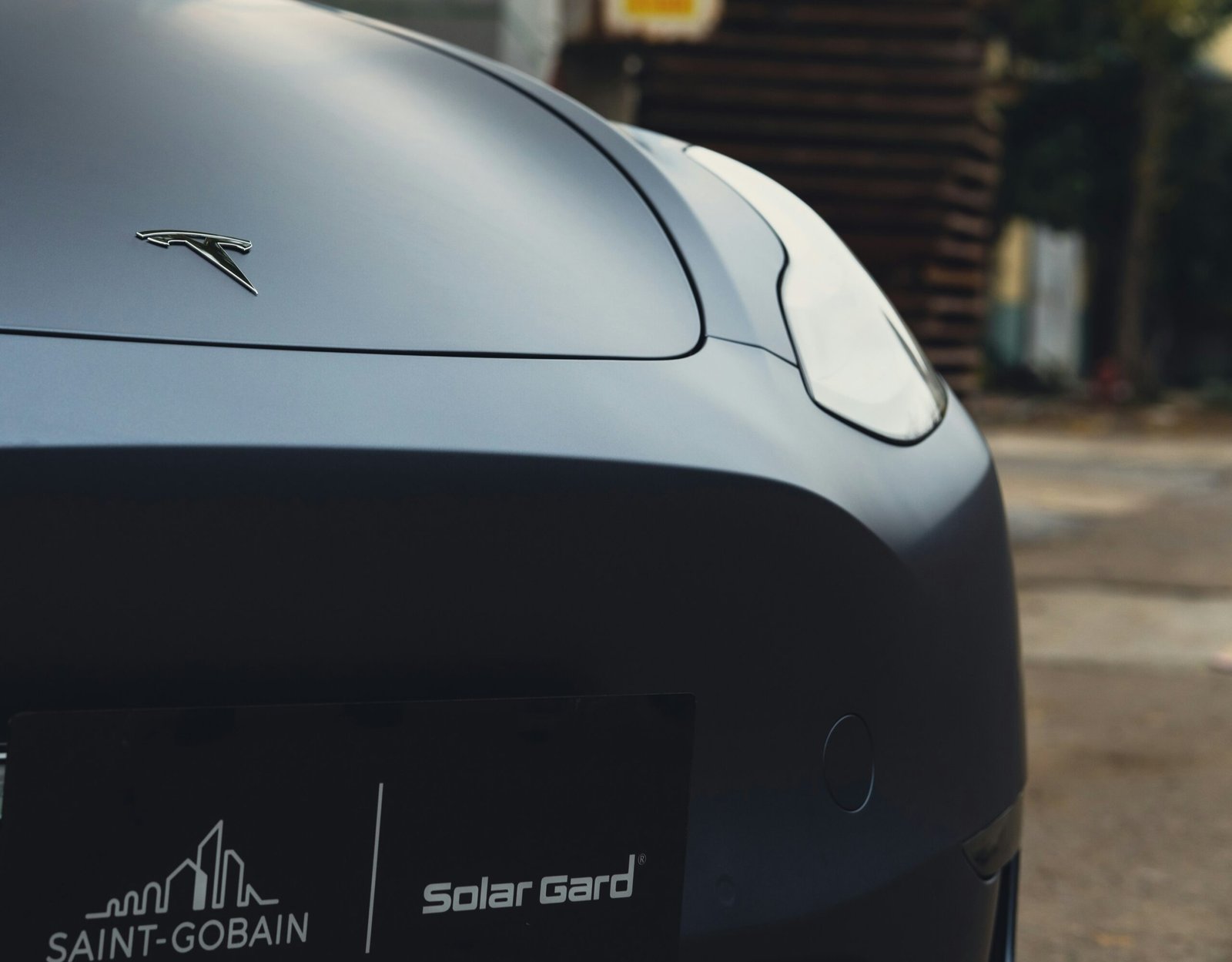 Une voiture électrique blanche branchée à une borne de recharge publique dans un parking ensoleillé, avec des panneaux solaires en arrière-plan.