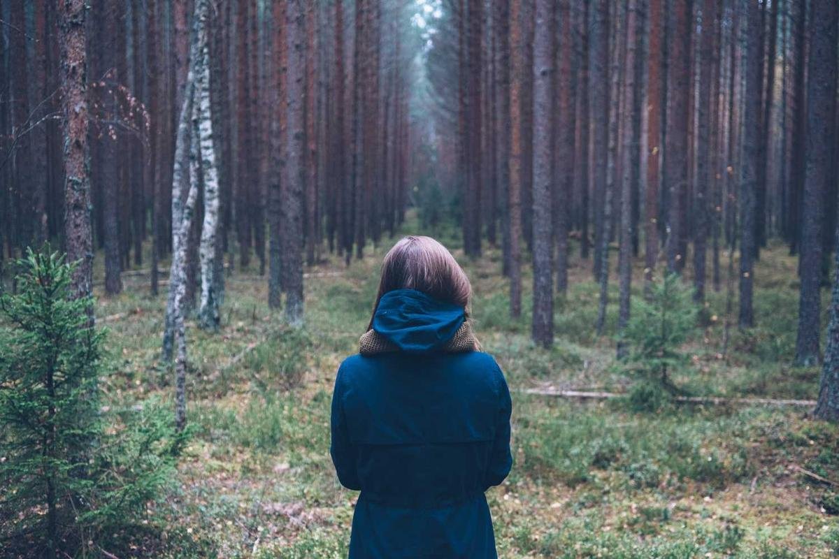 Woman facing forest of tall, thin trees.