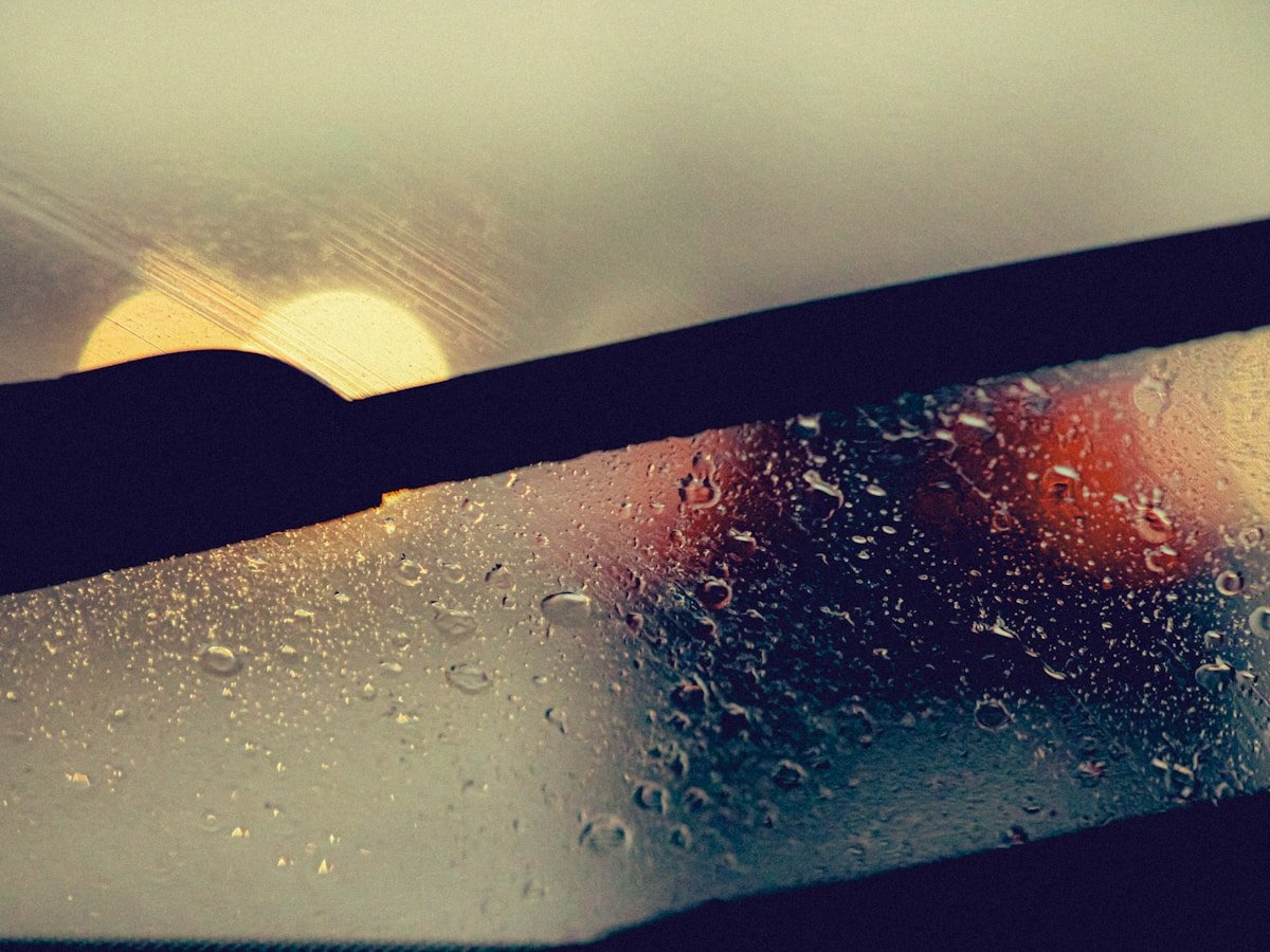Raindrops on a car windshield with sun and traffic lights.