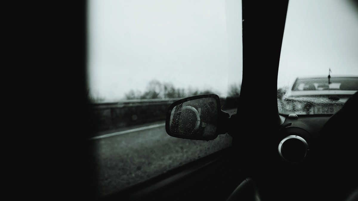 Paysage flou vu du rétroviseur d'une voiture par temps de pluie.