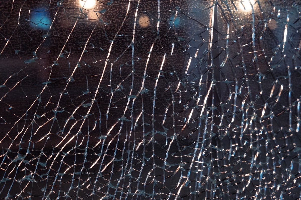 Verre brisé, fissures irrégulières, reflets lumineux, texture sombre, motif complexe.