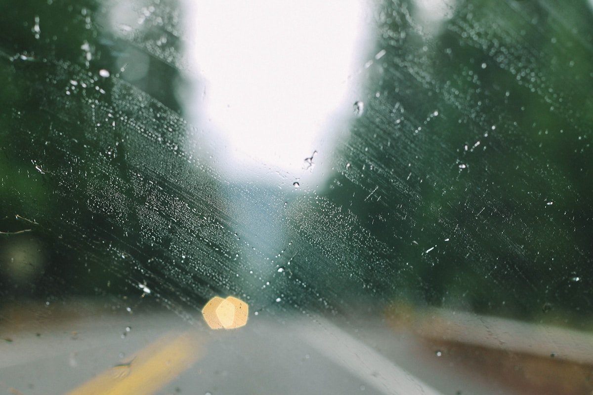 Gouttes de pluie sur un pare-brise flou avec des lumières floues à l'arrière-plan.