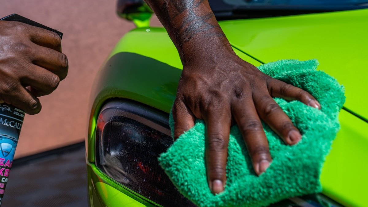 Mains noires tenant un chiffon vert sur une surface verte.